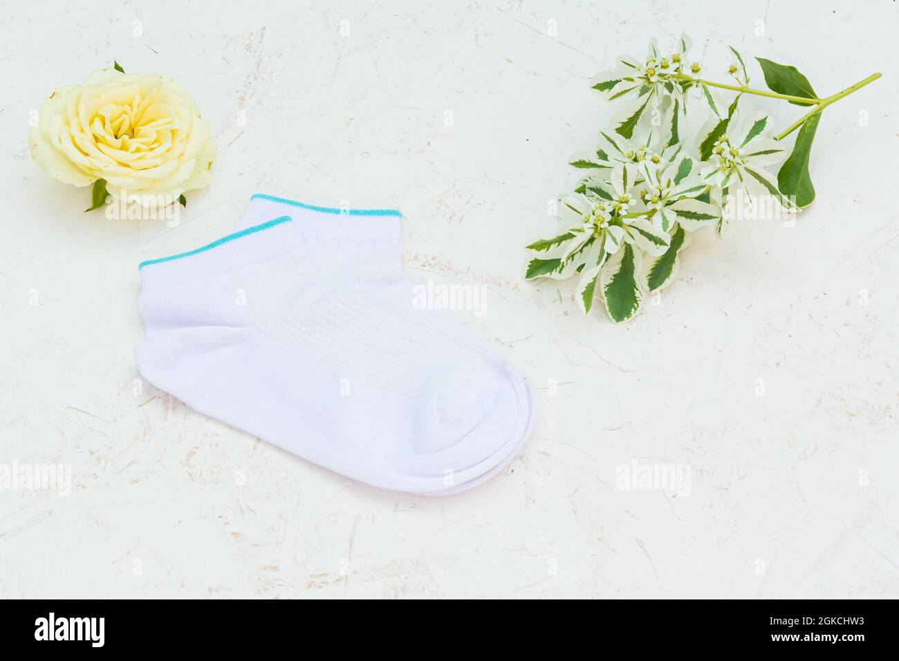 Paire de chaussettes blanches et boutons de fleurs sur fond blanc structuré, vue du dessus. Banque D'Images