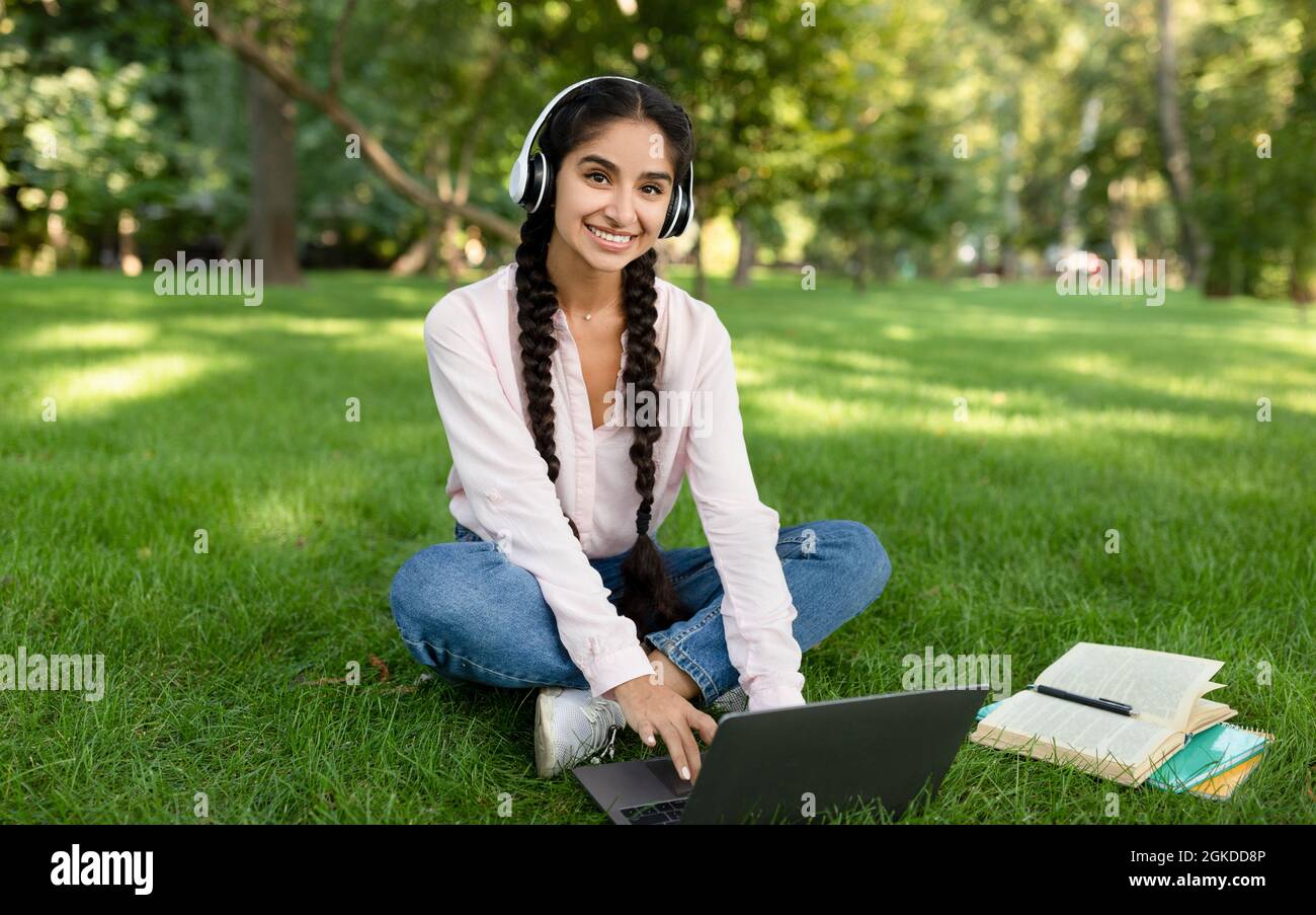 Une étudiante indienne qui utilise un ordinateur portable, apprend sur le campus universitaire, porte un casque et sourit à la caméra Banque D'Images