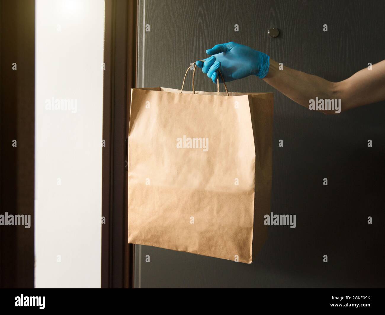 Sac en papier à main avec nourriture dans les portes, dans les gants médicaux, dans l'espace de copie. Livraison sécuritaire de l'épicerie, service de messagerie pendant la quarantaine du coronavirus. Banque D'Images