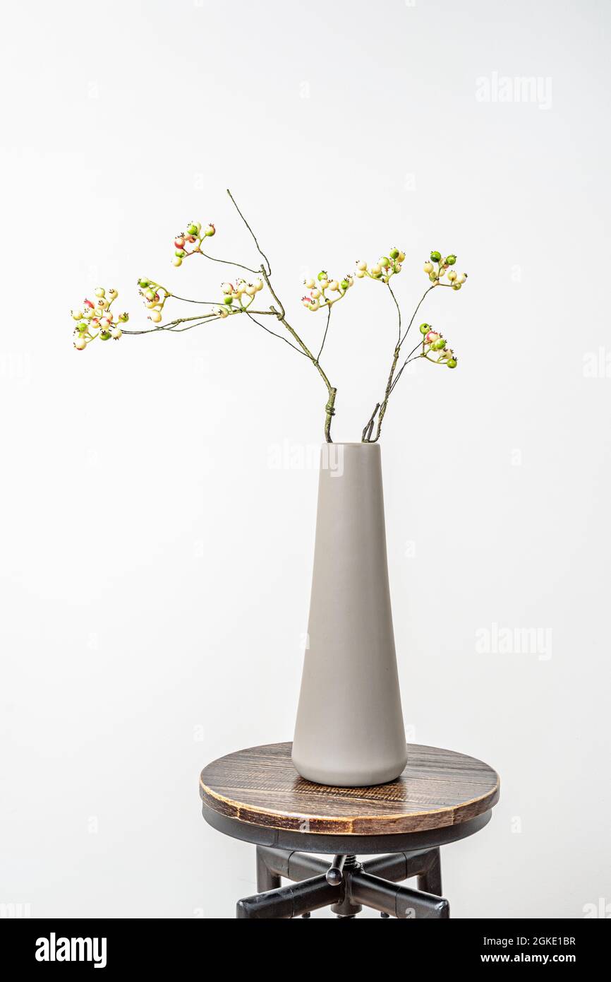 Vase cylindrique gris long avec branche décorative de myrtille jaune sur un tabouret industriel vintage Banque D'Images