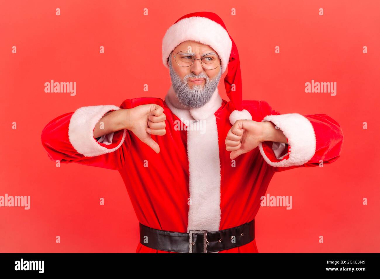 Homme âgé avec barbe grise portant le costume du père noël a l'expression de rire et de montrer les pouces vers le bas, exprimant la désapprobation, rétroaction négative. IND Banque D'Images