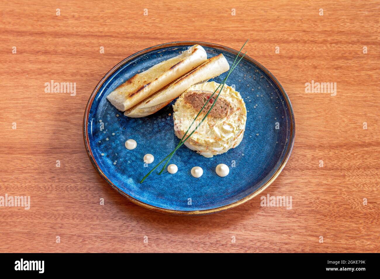 Salade russe préparée pour des tapas avec du thon en conserve et deux toasts de pain chaud sur une belle assiette bleue Banque D'Images