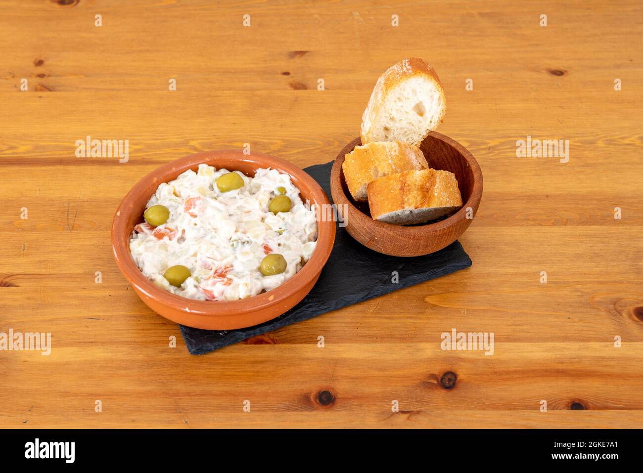 Dessus de salade russe aux olives avec un bol de pain sur une table en bois Banque D'Images