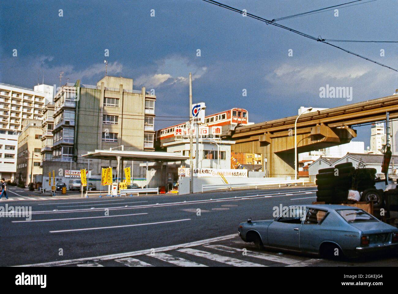 Un train monorail local sur le pont au-dessus d'une route, Tokyo, Japon c.1982. Le monorail de Tokyo a été ouvert en 1964 (pour les Jeux Olympiques de cette année-là). Il relie Hamamatsucho et l'aéroport d'Hameda. Les trains ont été construits par Hitachi au design allemand d'ALWEG. Il est considéré comme le monorail le plus occupé (et le plus rentable) au monde. Une station-service se trouve dans la rue ci-dessous. Cette image est tirée de la transparence couleur Agfa d'un photographe amateur – une photographie vintage des années 1980. Banque D'Images