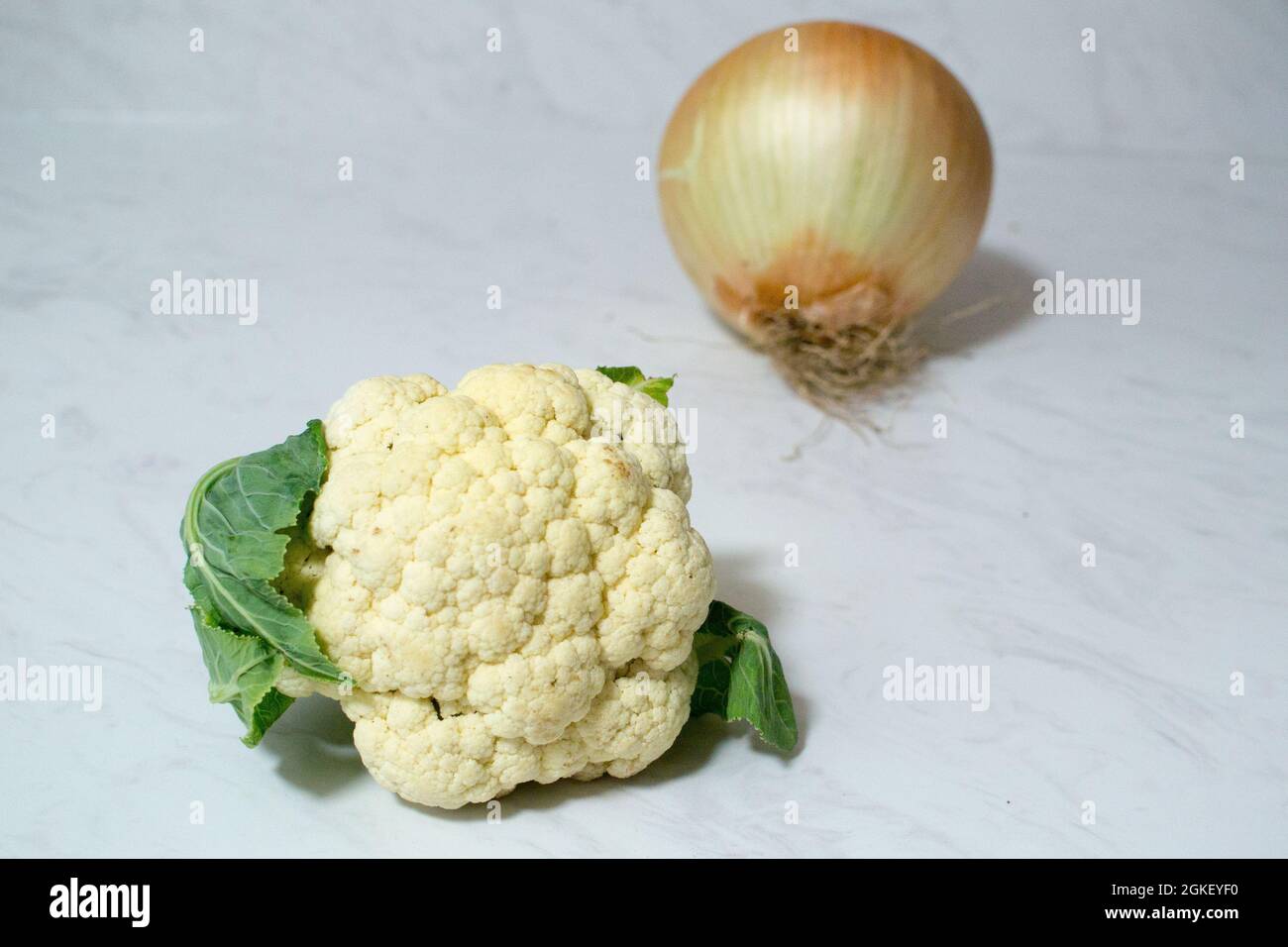 Un oignon géant, et/ou un minuscule chou-fleur sur une surface en marbre - un ou les deux légumes sont exceptionnellement petits ou étonnamment grands. L'oignon est plus grand que le cauli. Banque D'Images