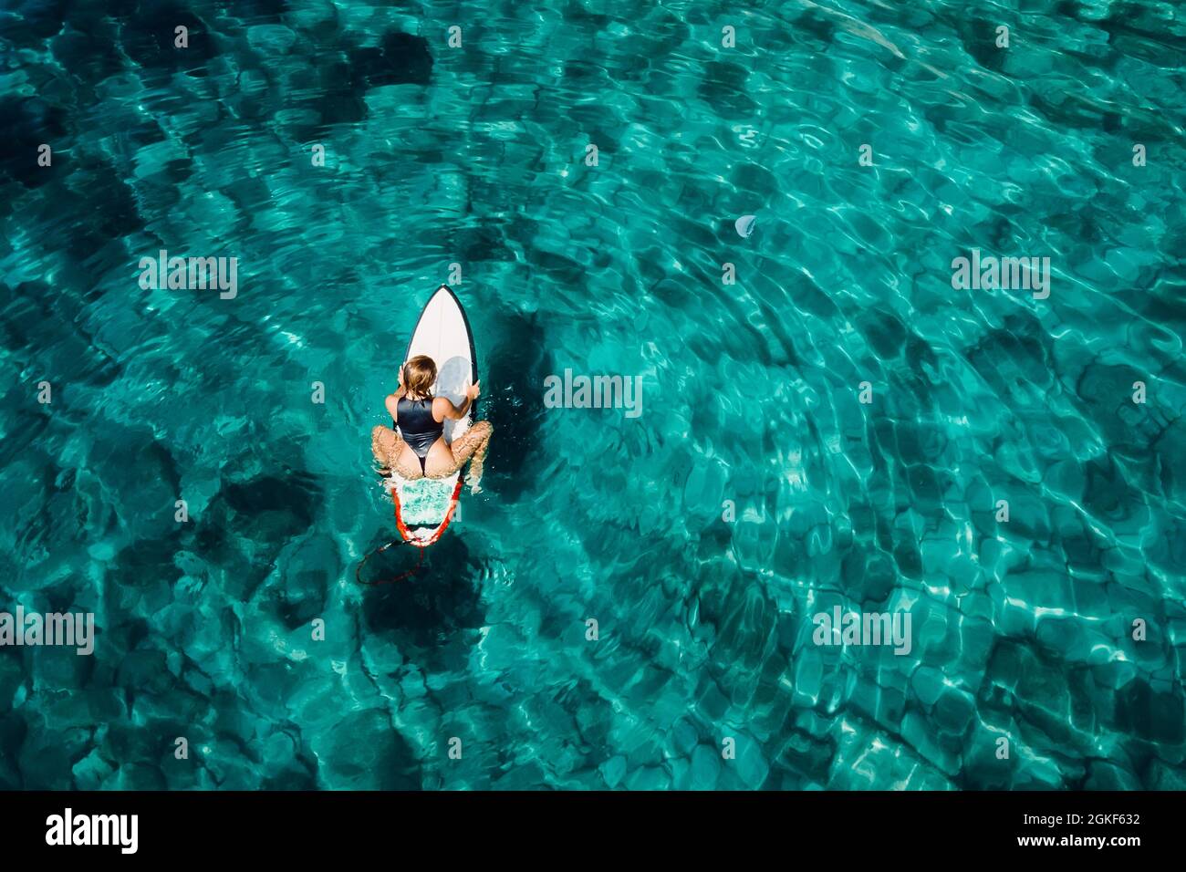 Une fille surfeuse assise sur une planche de surf dans un océan turquoise transparent. Vue aérienne avec une surfeuse Banque D'Images