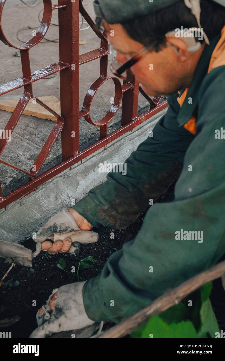 Les techniciens de construction avec aide auditive travaillant avec le revêtement de ciment, mélanger avec la truelle au travail latéral dans l'arrière-cour. Mortier de ciment en poudre mis sur la brique. REA Banque D'Images