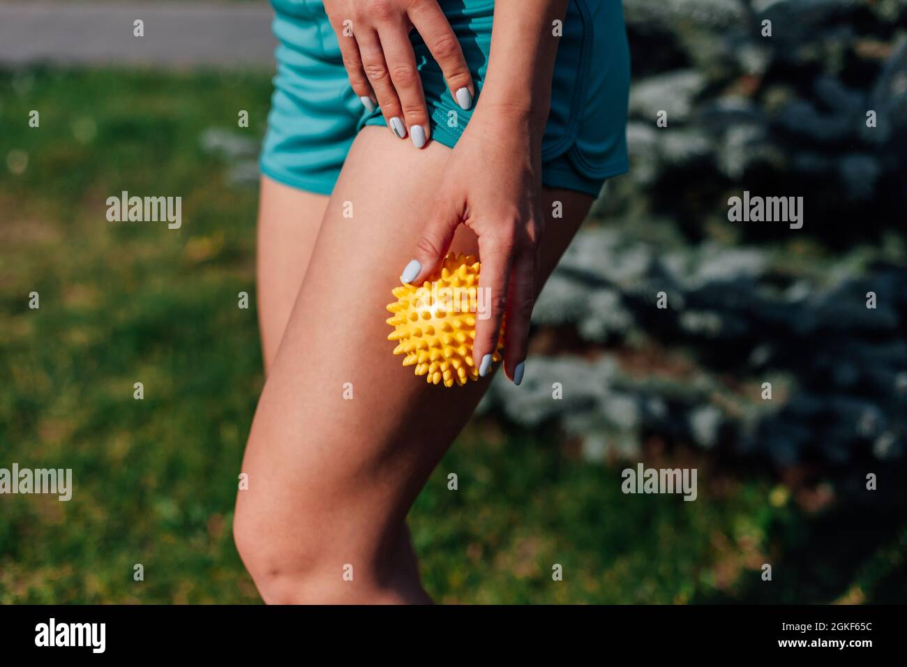 vue latérale du corps athlétique mince d'une jeune femme qui fait un massage de la hanche avec du ballon piquant dans le parc en été Banque D'Images