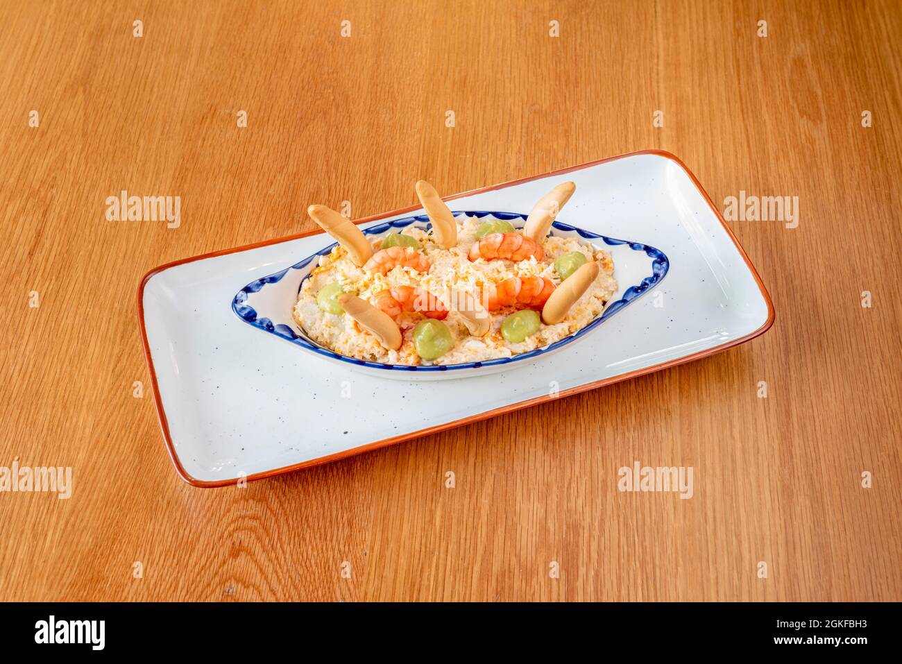 Salade russe aux croûtons, crevettes cuites et quelques touches d'avocat sur une jolie assiette à bord bleu Banque D'Images