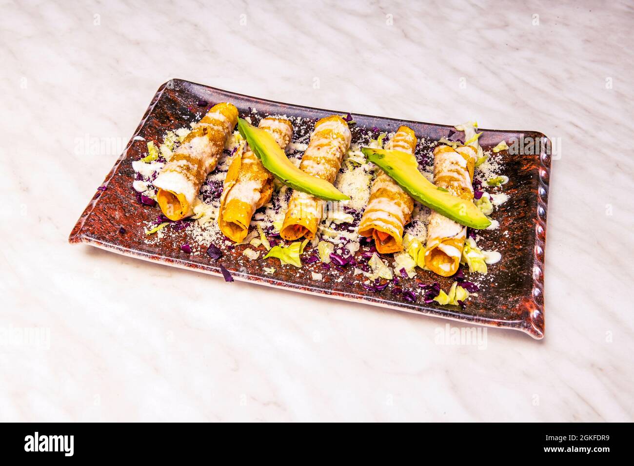 Assiette de délicieux flautas de poulet mexicain avec fromage à la crème et fromage râpé, avec tranches d'avocat et tortillas de maïs jaune Banque D'Images