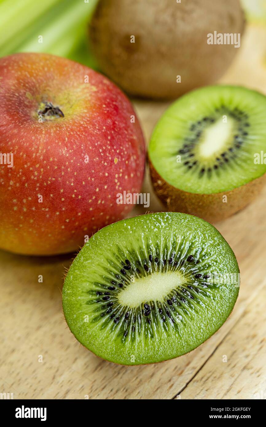 Gros plan de kiwi coupé en deux et plus de kiwis sur fond de pomme rouge sur fond de bois clair Banque D'Images