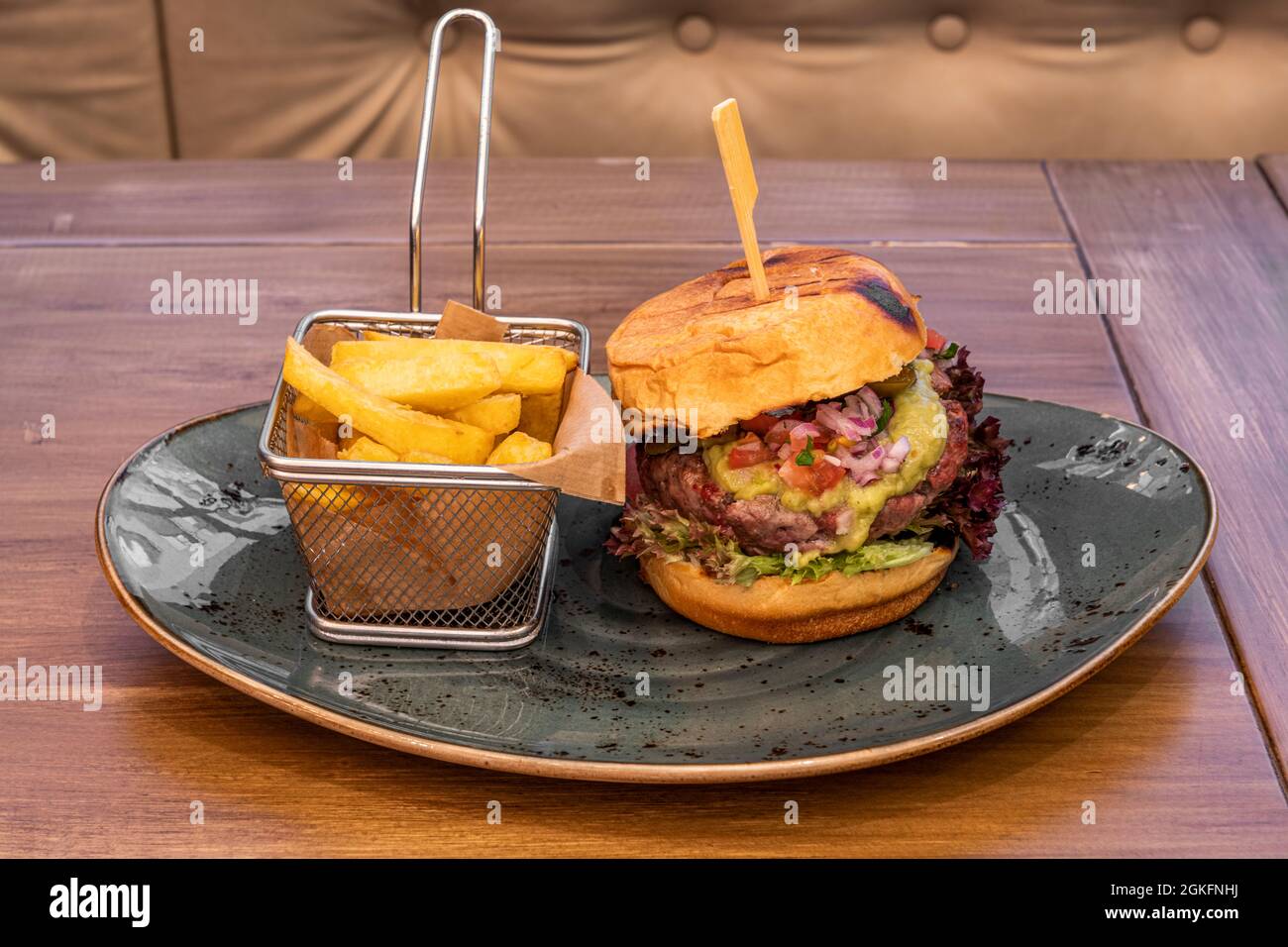 Hamburger mexicain avec 200 grammes de bœuf, guacamole et pico de gallo et garniture de pommes de terre dans une friteuse métallique sur une assiette bleue Banque D'Images