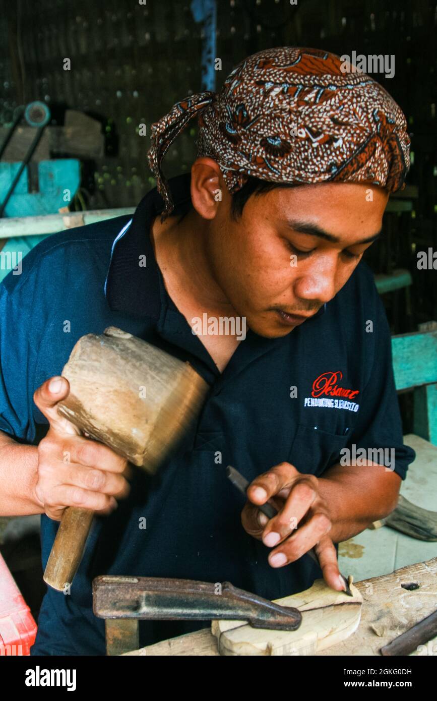 Un jeune homme sculptant du bois pour faire un warangka ou un scabard d'un keris. Banque D'Images