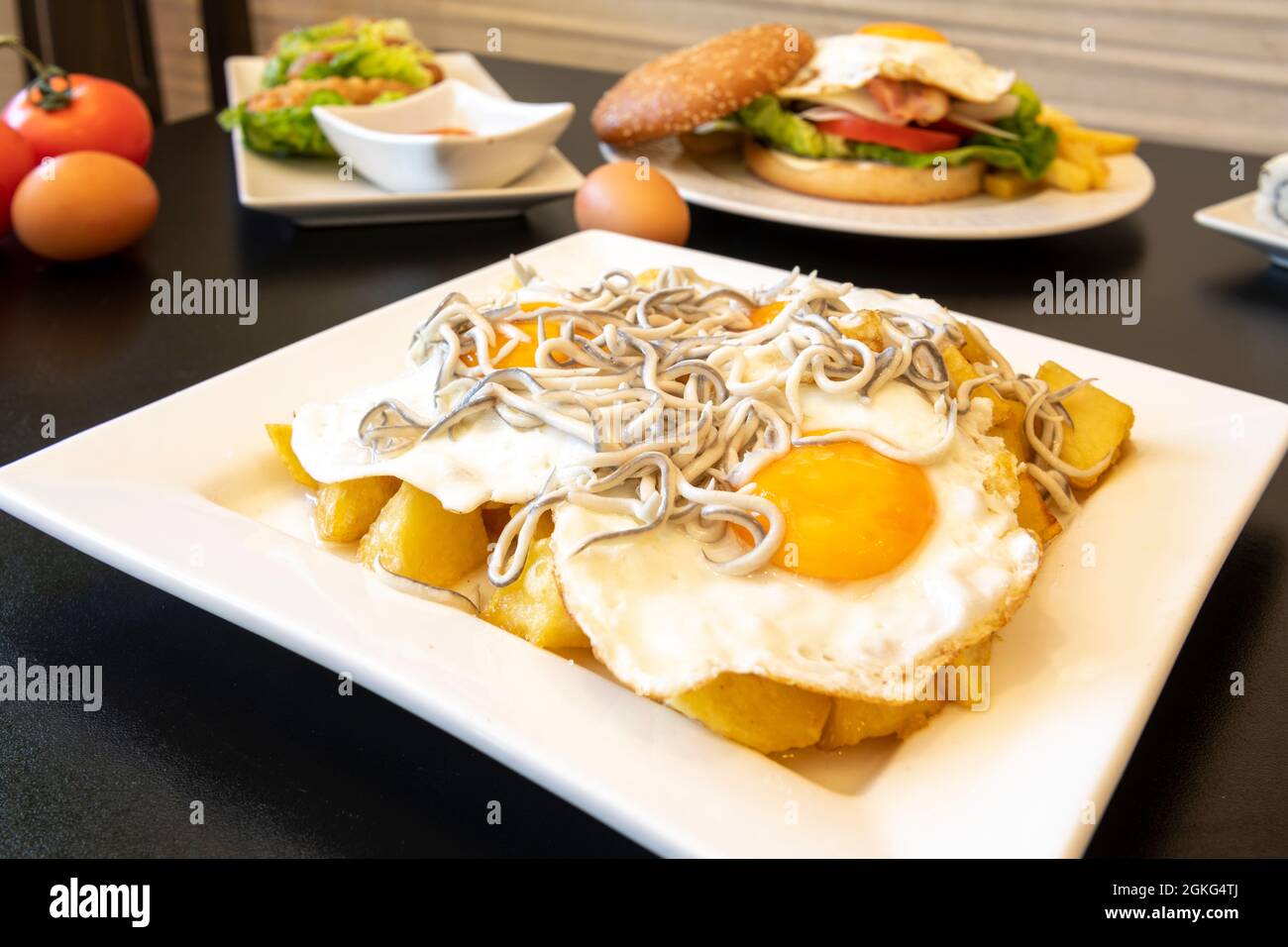 Tapa typiquement espagnol d'œufs cassés avec anguilles à partager sur une table de restaurant avec d'autres plats en arrière-plan Banque D'Images