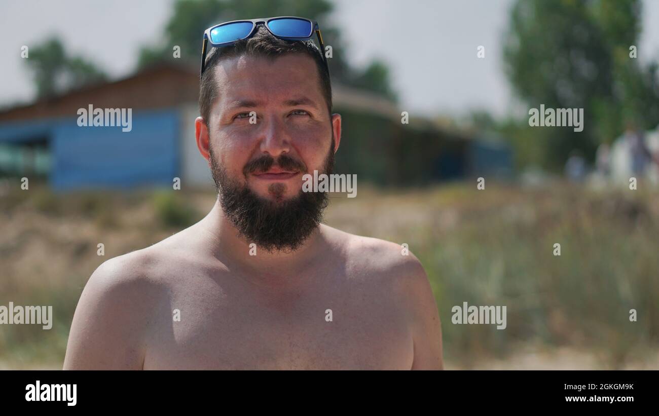 Un portrait authentique d'un jeune homme barbu confiant regardant l'appareil photo. Vue rapprochée d'un jeune homme naturel sur la plage. Banque D'Images
