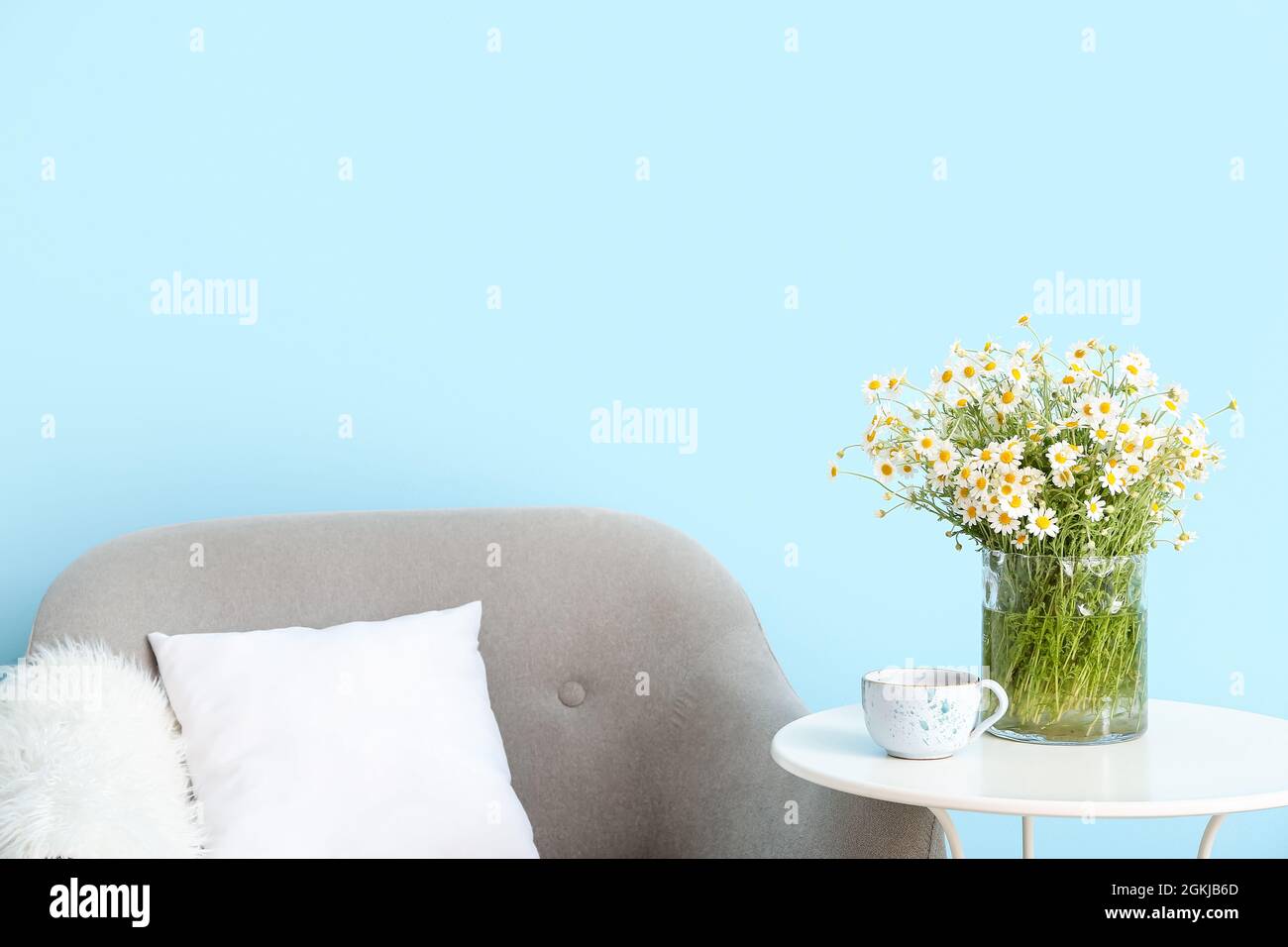 Vase avec des chamomiles et une tasse de thé sur la table près du mur de couleur Banque D'Images