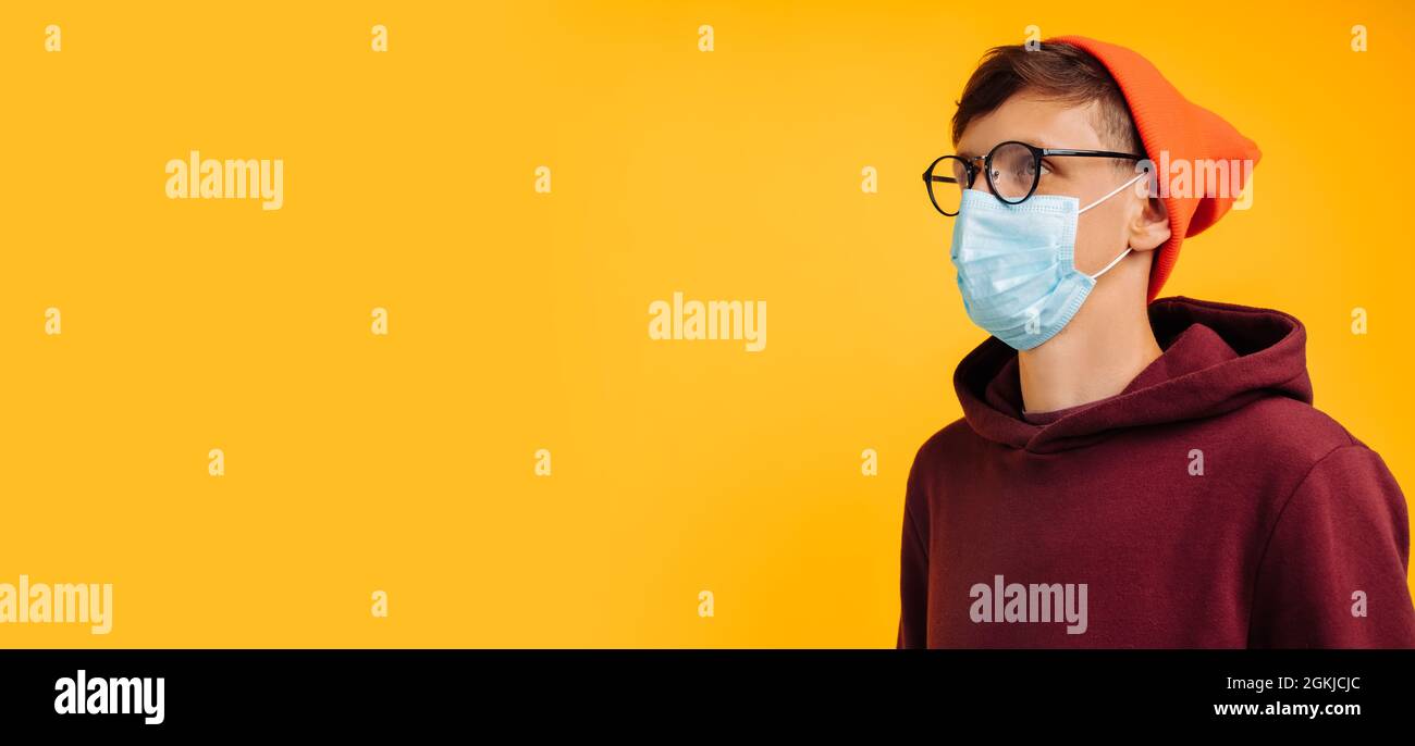 beau homme dans un masque de protection. en lunettes et un chapeau orange et un sweat-shirt rouge, souriant à l'appareil photo, sur fond jaune, heureux vacciné Banque D'Images