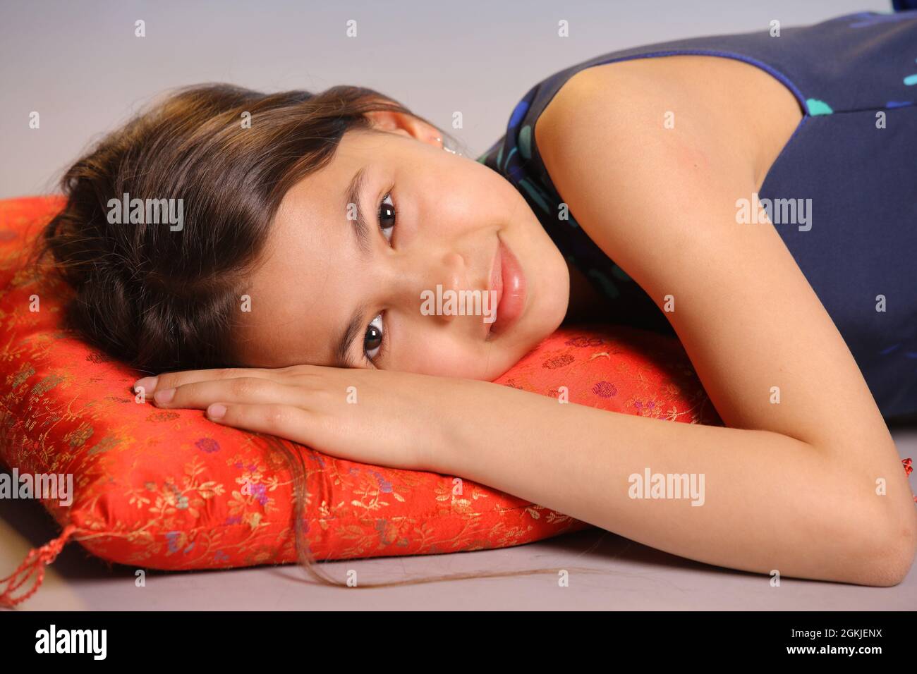 Portrait d'une adorable adolescente de 12 ans aux cheveux foncés. Elle se trouve sur un oreiller rouge et sourit. Banque D'Images