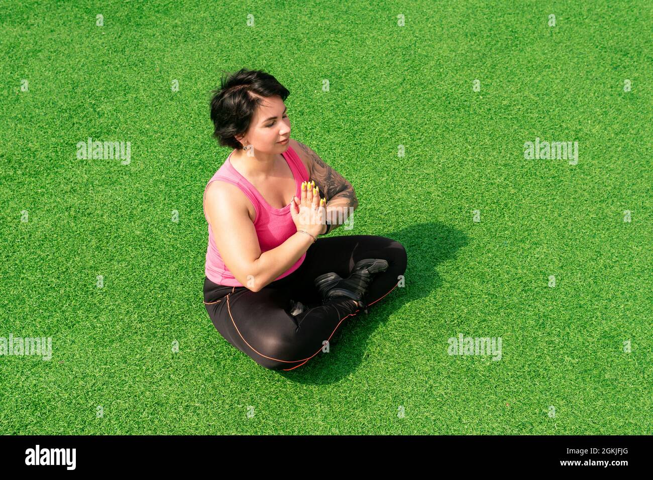 une jeune femme robuste médite sur la pelouse verte après avoir fait de l'exercice Banque D'Images