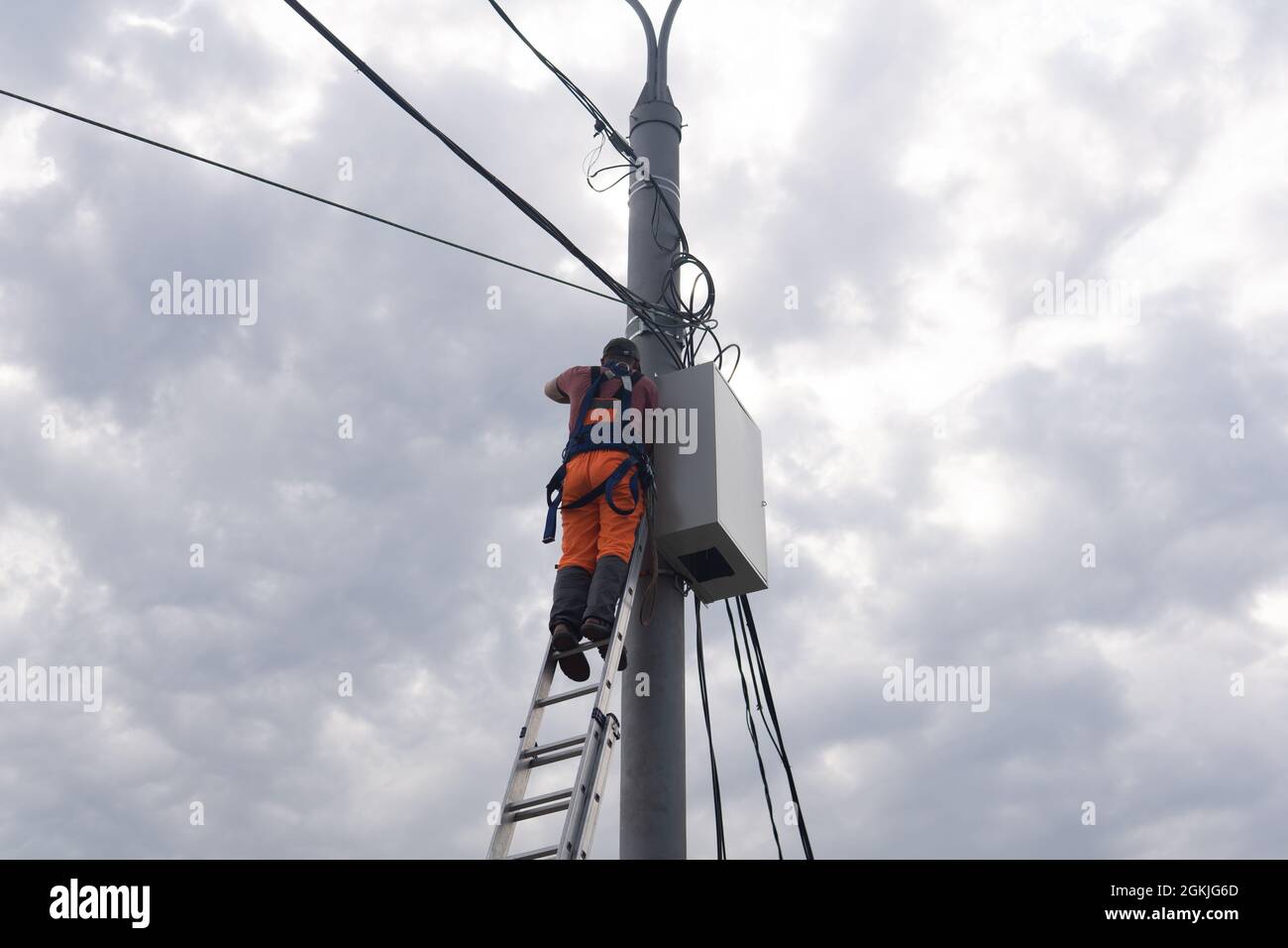 Perm, Russie - 25 août 2021 : un électricien ou un électricien de télécommunications travaille sur la pose d'un câble au sommet d'un poteau téléphonique Banque D'Images