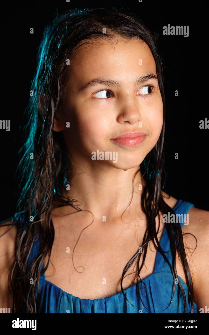 Portrait en gros plan d'une jeune fille de brunette gaie et lumineuse avec des cheveux mouillés sur un fond noir. Une adolescente de 12 ans vêchée d'une robe bleue m'a attrapée Banque D'Images