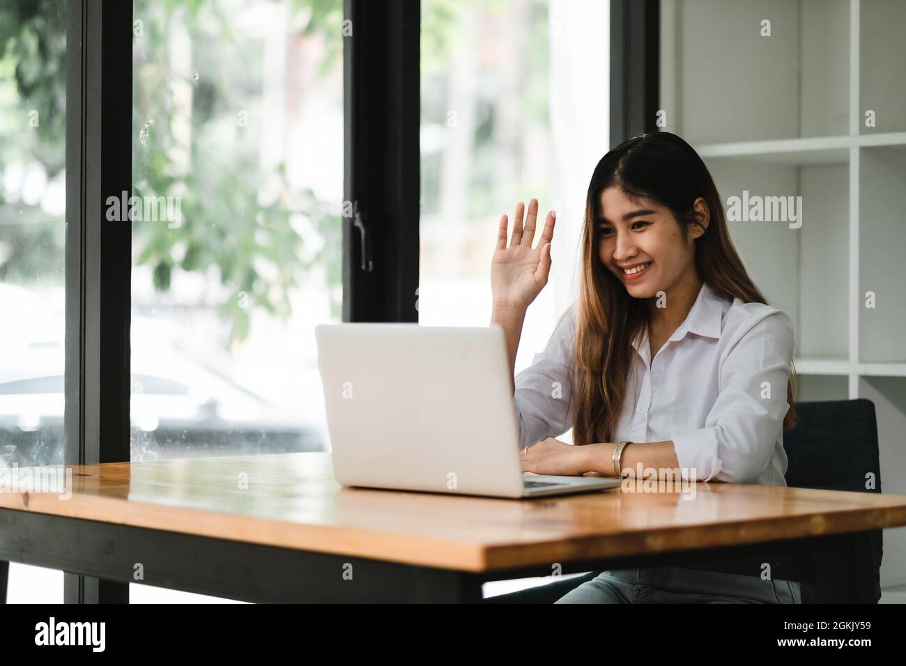 Une jeune fille asiatique souriante qui parle et se fait un bonjour lors d'un appel vidéo en ligne via un ordinateur portable, assis dans un café. Femme d'affaires gaie ayant Banque D'Images