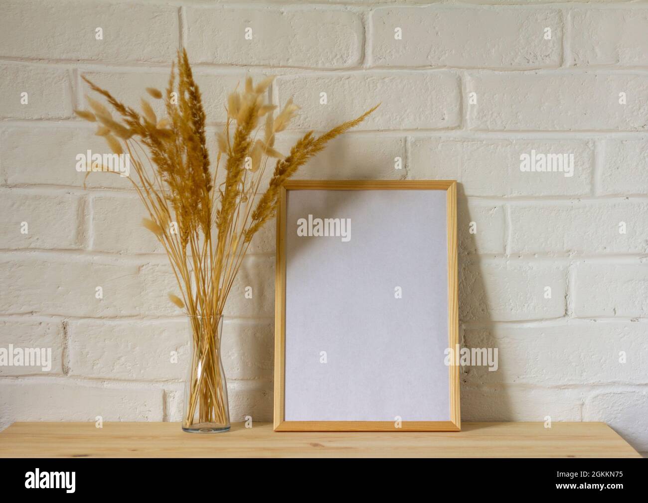 Une maquette d'un cadre photo vide et d'un bouquet d'automne d'herbes séchées dans un vase transparent sur une table en bois avec une copie de l'espace Banque D'Images