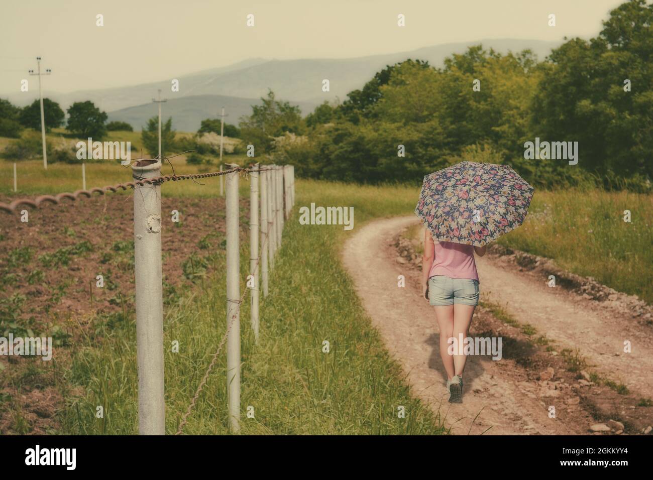 Fille avec un parapluie marchant sur une route de terre Banque D'Images