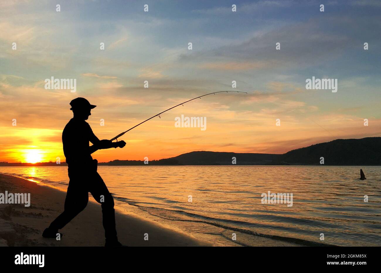 Un jeune homme pêche sur un lac au coucher du soleil Banque D'Images