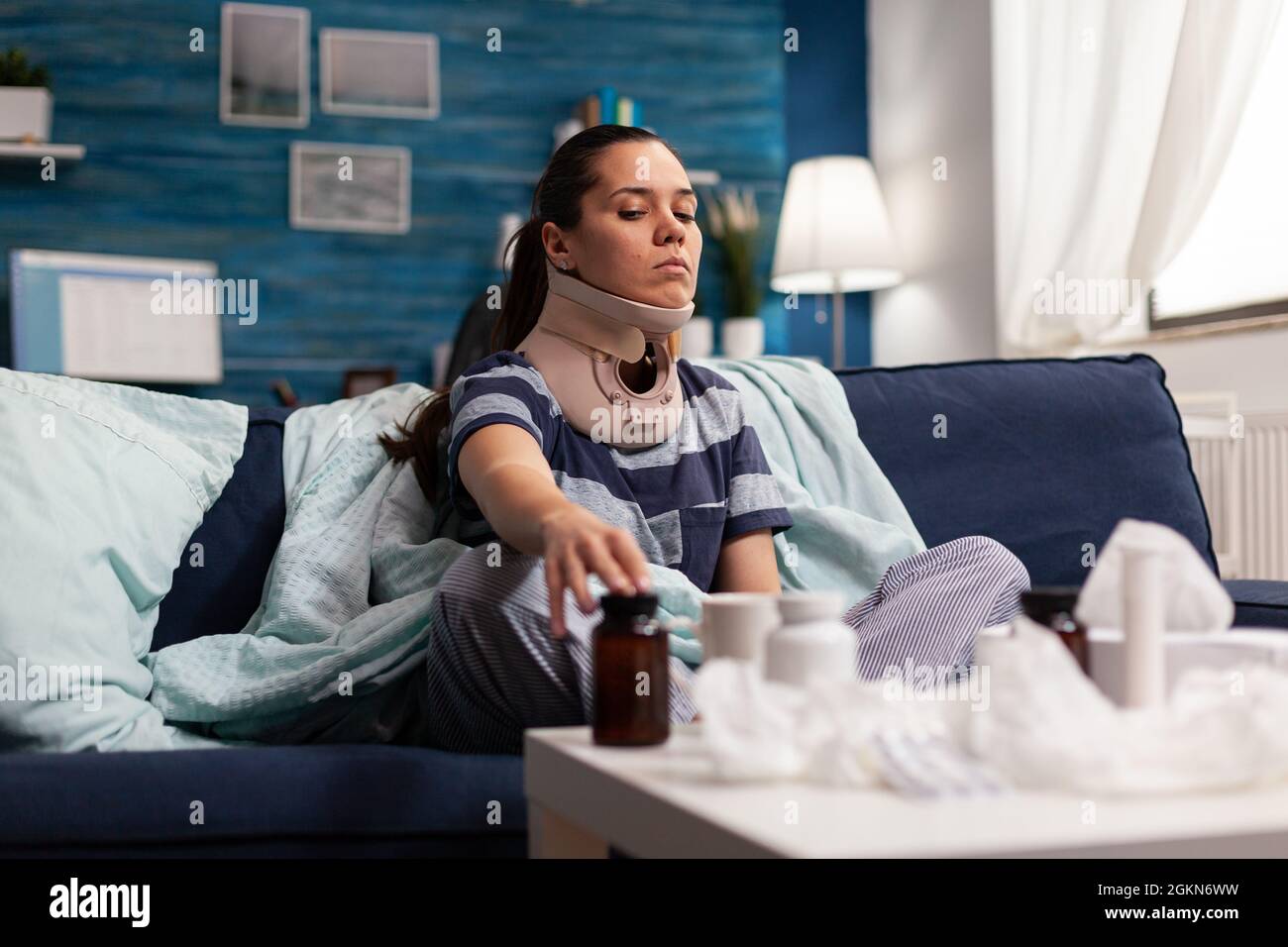 Femme avec col cervical assis sur un canapé souffrant de douleur de colonne vertébrale. Jeune caucasien avec une blessure physique prenant un médicament contre la douleur après un accident du dos, avec une gêne Banque D'Images