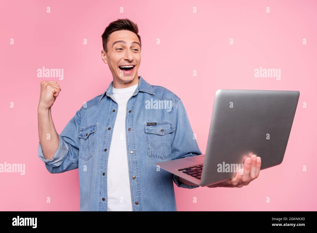 Photo de sourire excité fou gai gars soulever les poings dans la victoire tenir homme d'affaires d'ordinateur portable isolé sur fond de couleur rose Banque D'Images