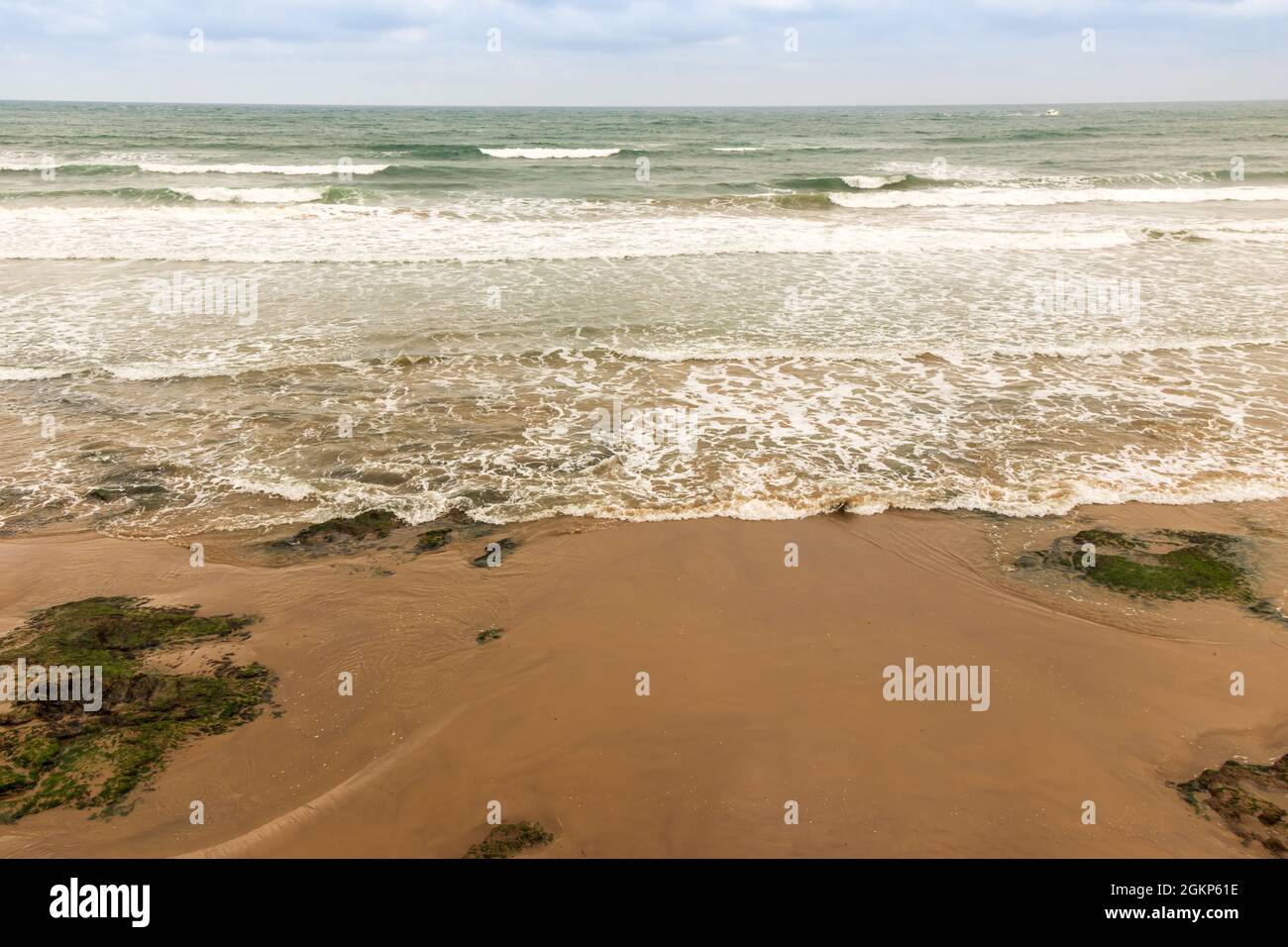 Vagues de mer doucement roulantes et moussantes sur une rive sablonneuse. Banque D'Images