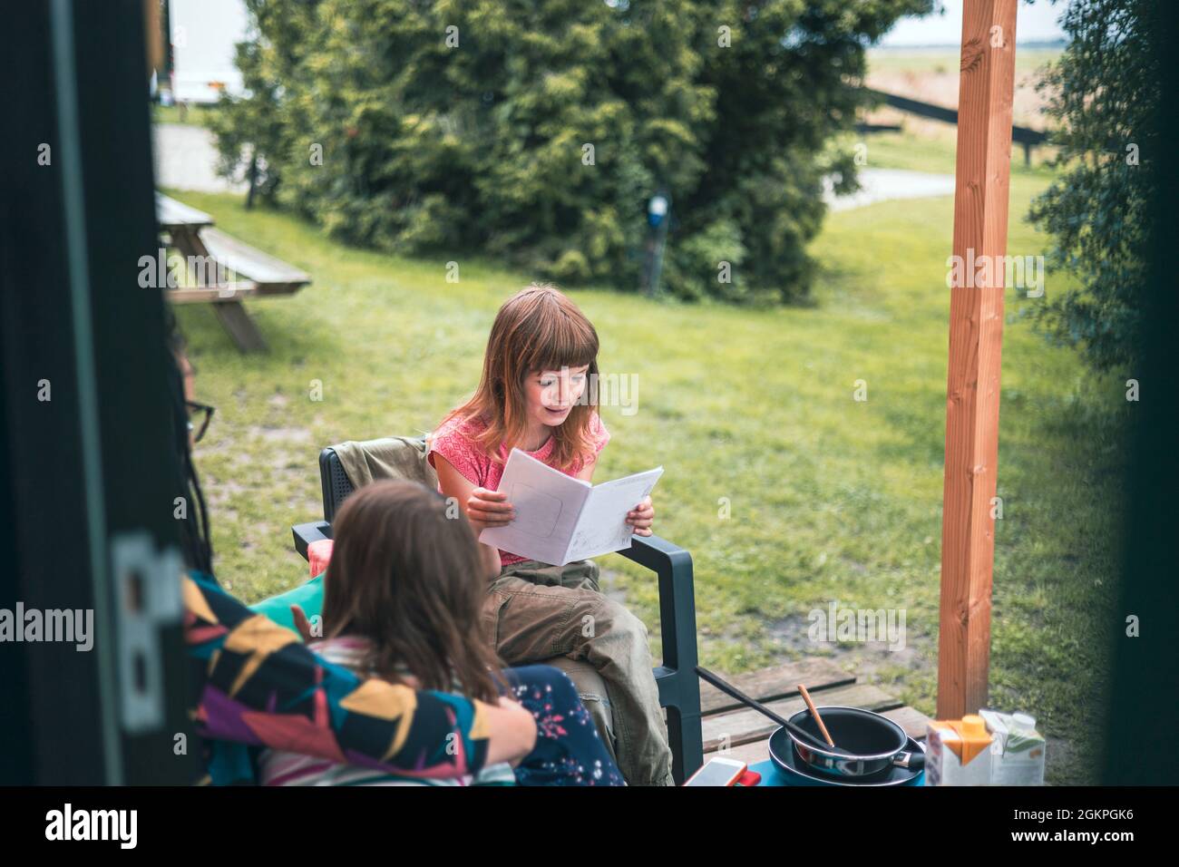 Fille lisant en face de la cabine en bois au camping Banque D'Images
