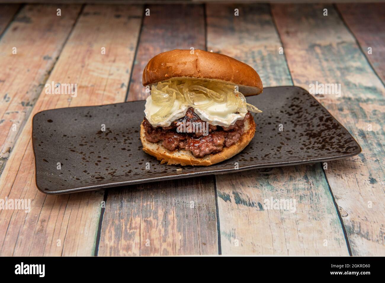 Hamburger avec double boeuf, double fromage de chèvre et oignon caramélisé sur un plateau noir Banque D'Images