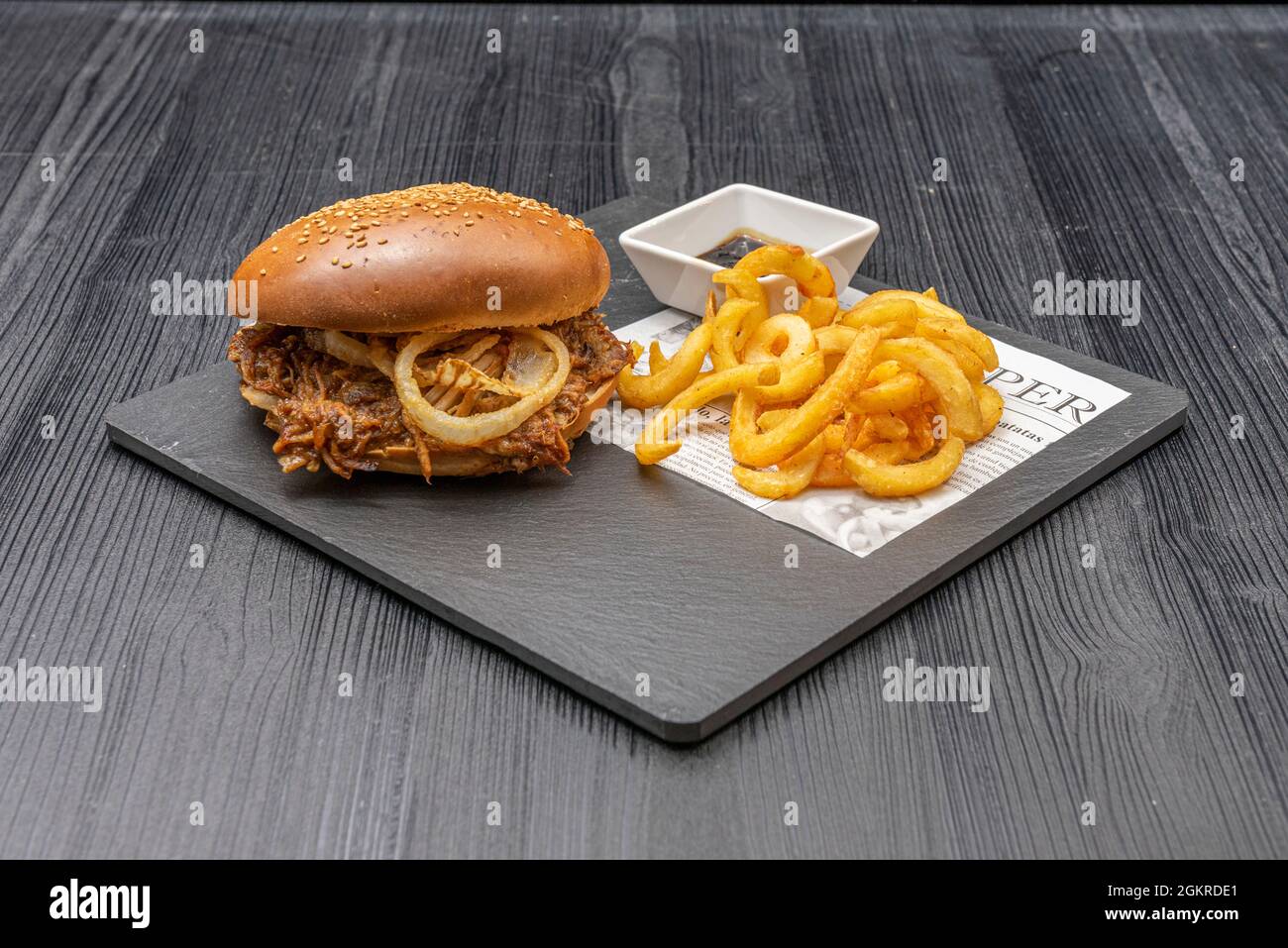 Hamburger au porc tiré avec rondelles d'oignon blanc croustillant, pain aux graines, frites et sauce barbecue Banque D'Images