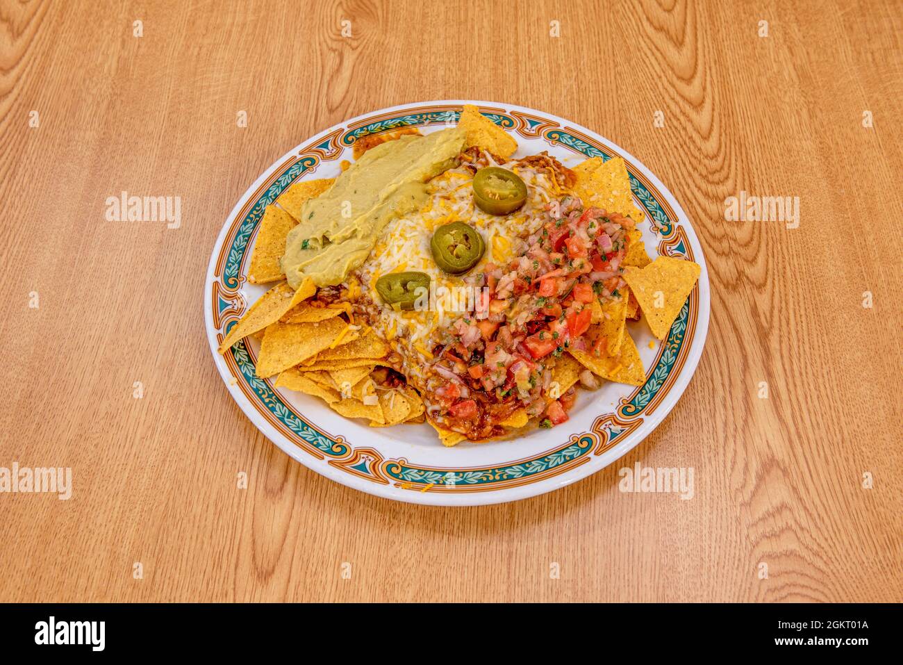 Assiette de nachos de maïs mexicain avec beaucoup de fromage, beaucoup de  guacamole et beaucoup de pico de gallo sur plaque blanche avec bordure et  table en bois Photo Stock - Alamy