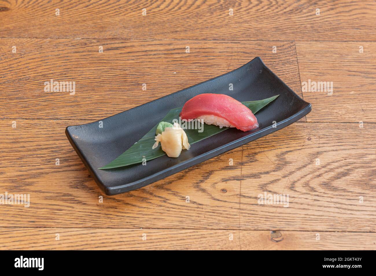 Morceau de nigiri de thon rouge de haute qualité servi sur une feuille de banane sur une assiette noire avec wasabi et ginseng Banque D'Images