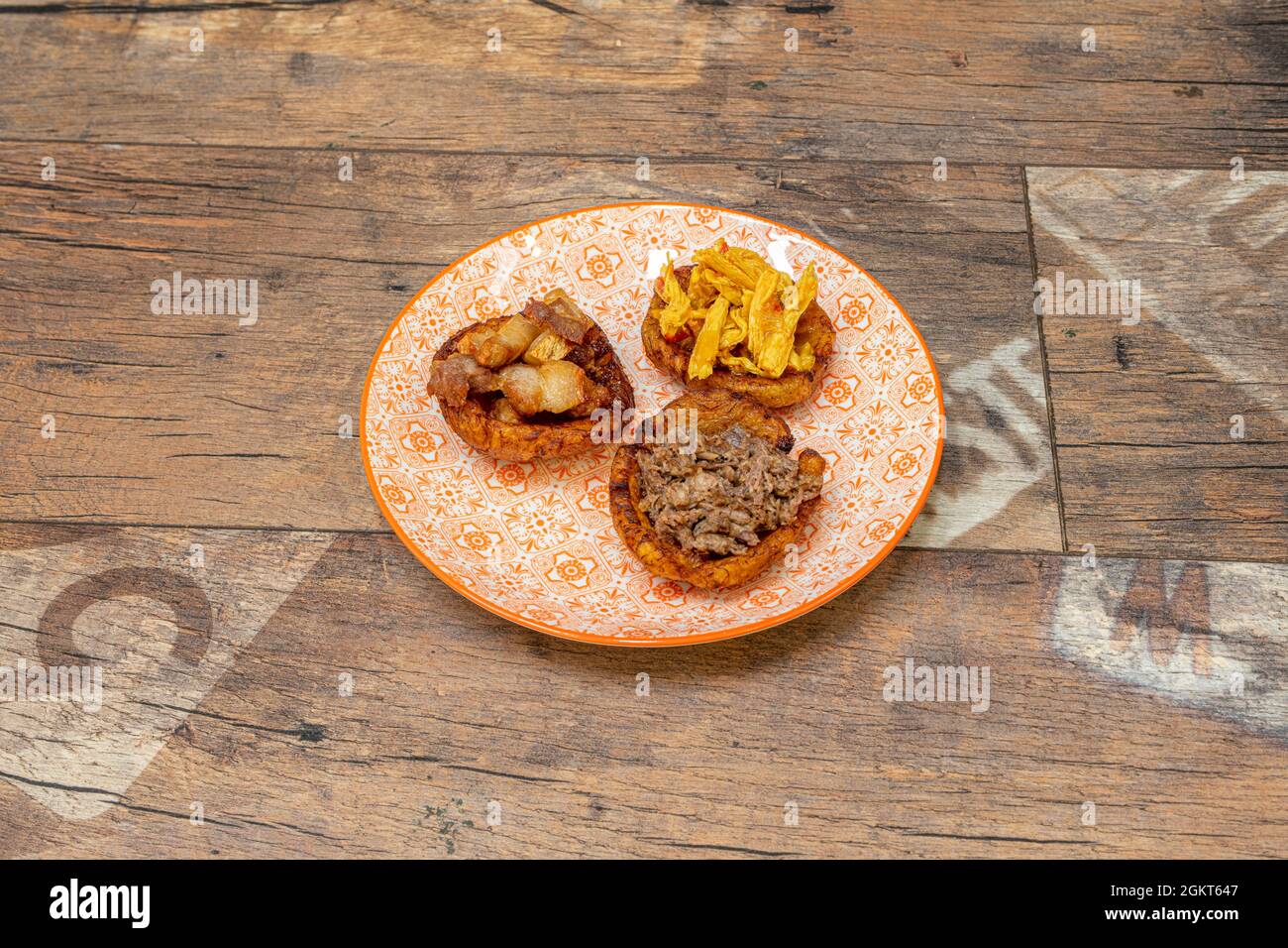 Assortiment vénézuélien Patacon avec chicharrones, viande de poulet et viande déchiquetée dans une belle assiette de tons orange Banque D'Images