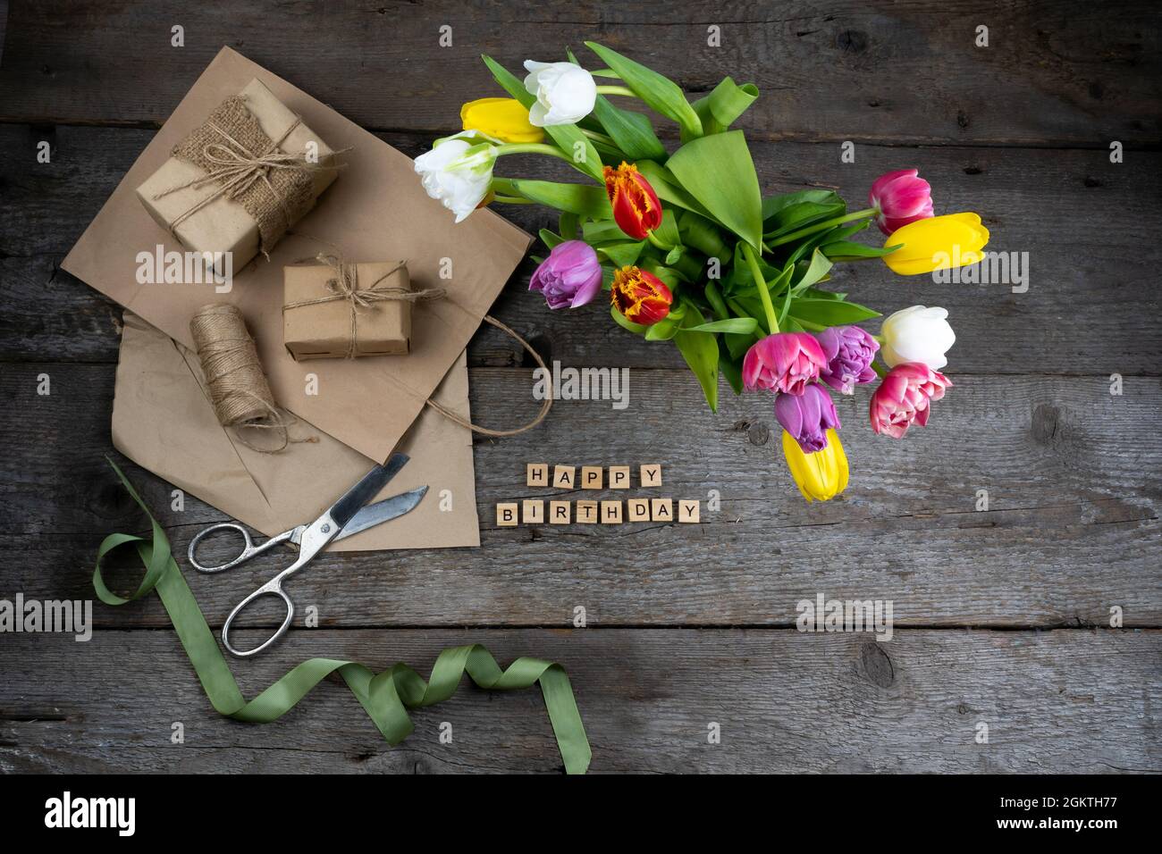 Inscription joyeux anniversaire en lettres de bois. Emballage cadeau. Mélange de fleurs de tulipes de printemps. Arrière-plan avec fleurs tulipes gros plan différentes couleurs Banque D'Images