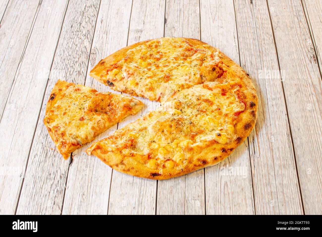 Petite pizza bien cuite à quatre fromages avec une tranche découpée sur une table en bois blanc Banque D'Images