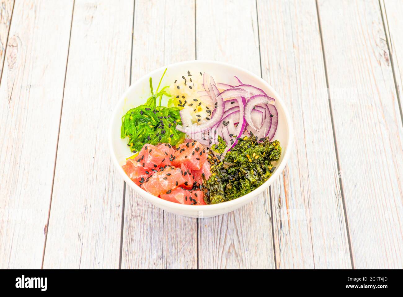 Assiette à pique de thon rouge hawaïen avec oignons rouges en rondelles, salade d'algues wakame, graines de sésame et pavot sur table blanche en bois Banque D'Images