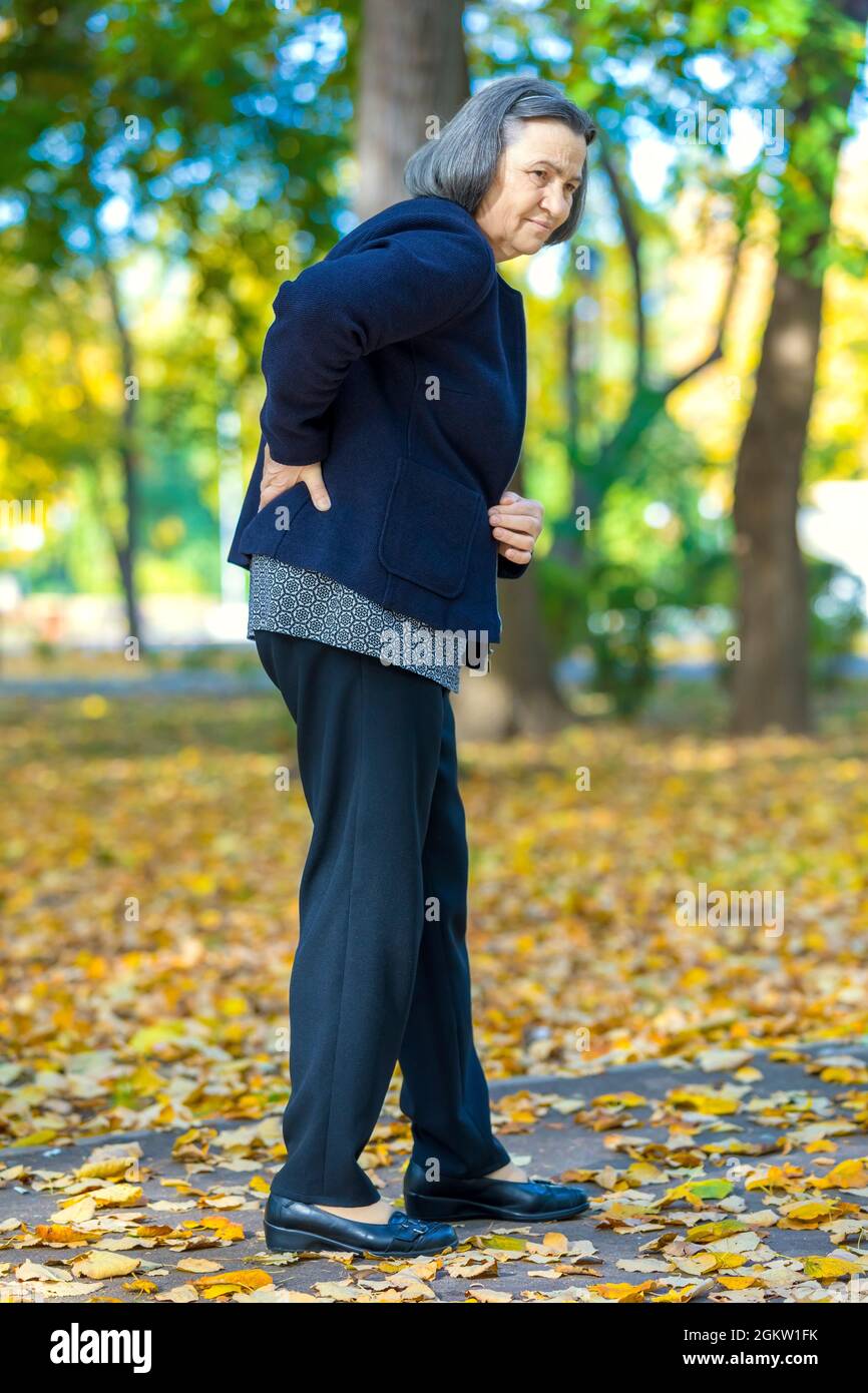Femme âgée souffrant de mal de dos à l'extérieur dans le parc d'automne. Banque D'Images