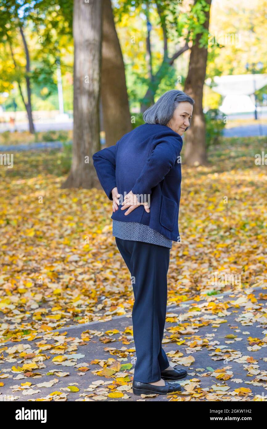 Femme âgée souffrant de mal de dos à l'extérieur dans le parc d'automne. Banque D'Images