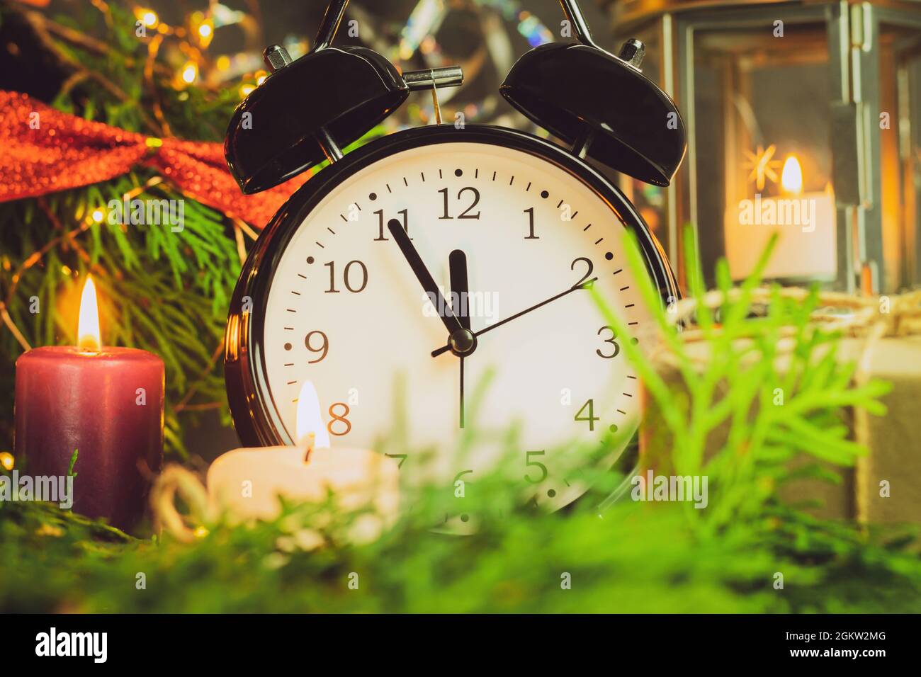 Une horloge dans les décorations du nouvel an est enveloppée de branches d'épinette et de lumières colorées. L'horloge indique l'heure : de cinq minutes à minuit. Arrière-plan W Banque D'Images
