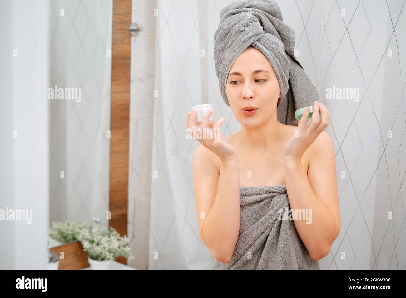 Femme dans la salle de bains tient un pot de crème hydratante pour le visage et le corps. Banque D'Images