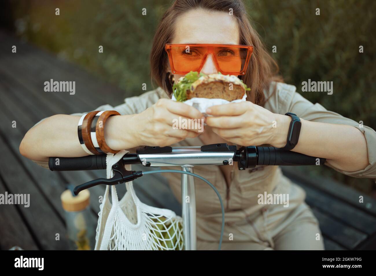 femme tendance de 40 ans en lunettes de soleil et en combinaison avec sac à  ficelle, scooter et sandwich assis à l'extérieur de la ville Photo Stock -  Alamy
