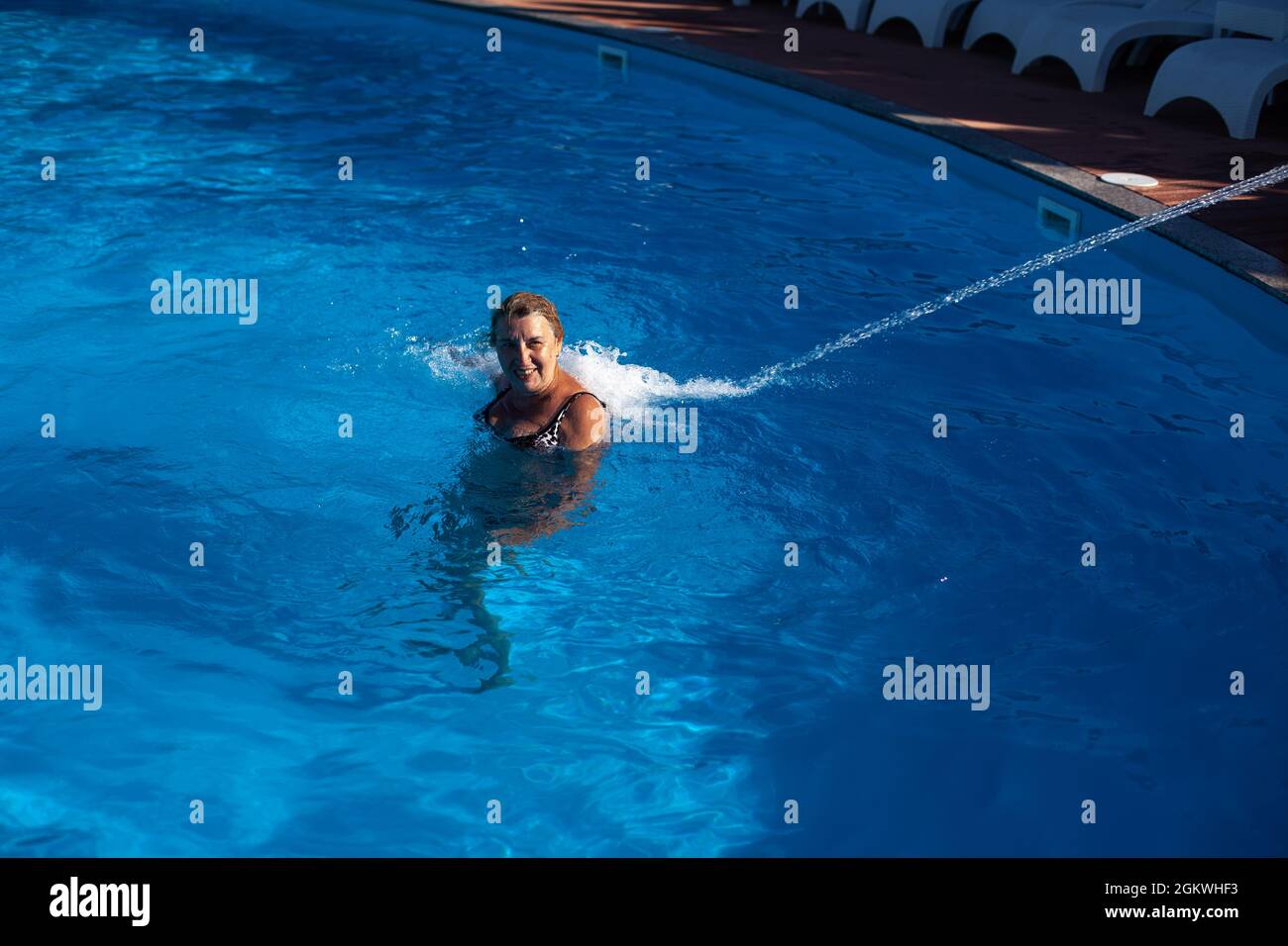 Une femme adulte souriante bénéficie d'un hydro-massage du dos et du cou avec un jet d'eau dans la piscine du spa lors d'un voyage Banque D'Images