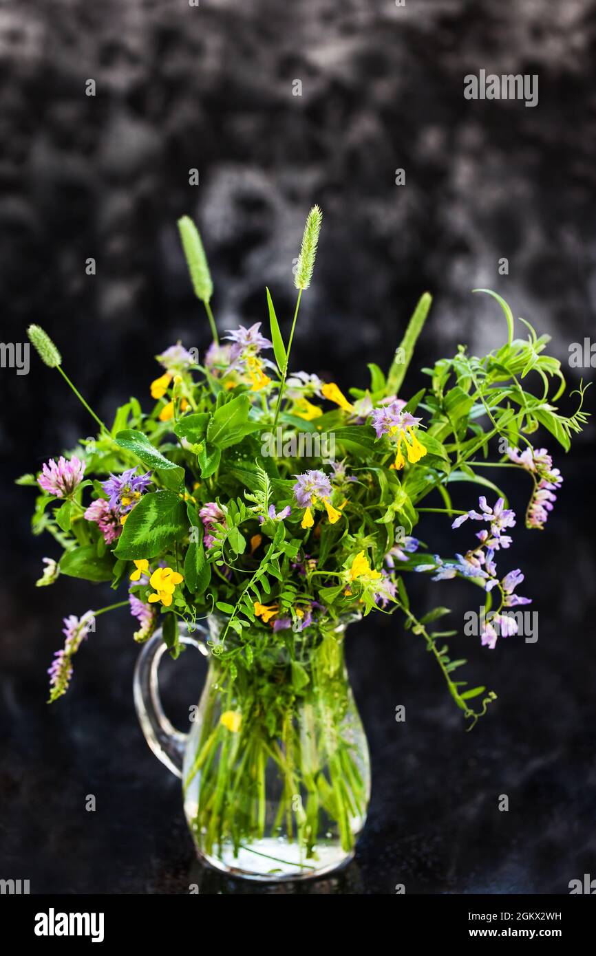 Bouquet de fleurs sauvages dans un pot en verre sur fond sombre Banque D'Images