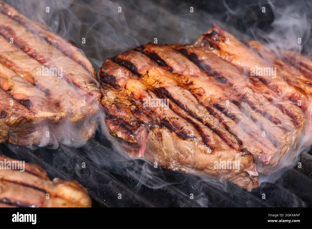 Gros plan sur des steaks de bœuf à la rivée et fumant sur une grille extérieure à feu ouvert avec grille en fonte métallique, vue en grand angle Banque D'Images