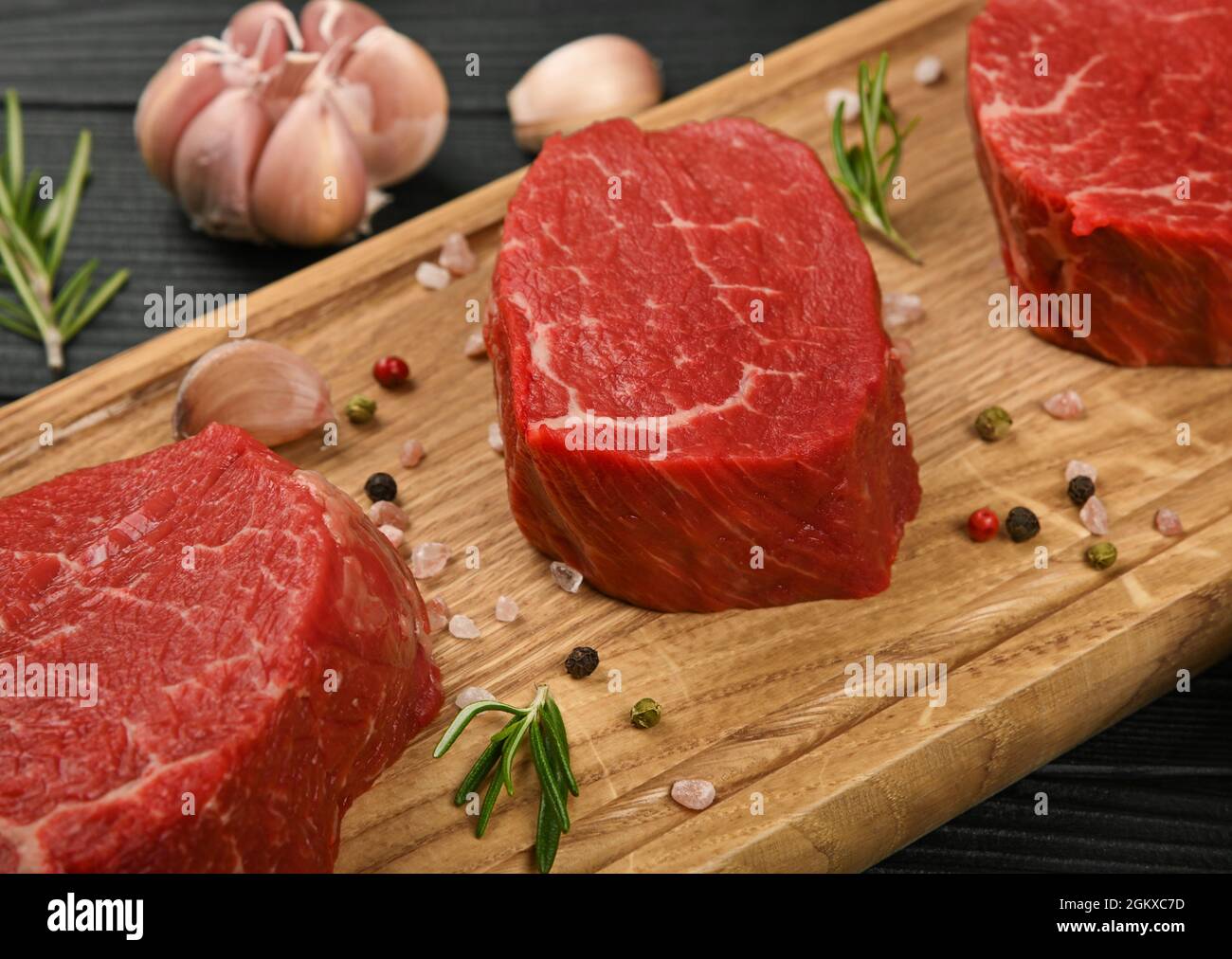 Gros plan sur trois steaks de bœuf maillé de qualité supérieure ou filet mignon sur une planche à découper en bois de chêne brun, avec des épices, sur une table en bois noir Banque D'Images